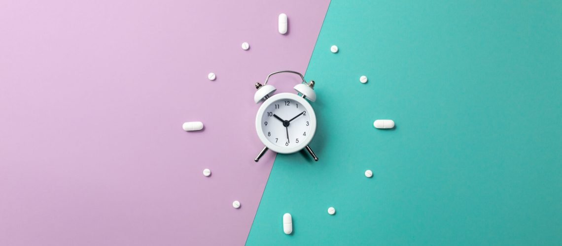 Pills, tablets and white alarm clock on colorful background. Medical and health concept in minimal style. Top view