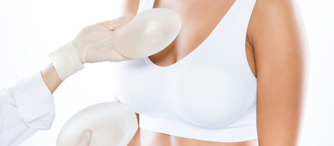 Portrait of female doctor choosing mammary prosthesis with her patient over white background.